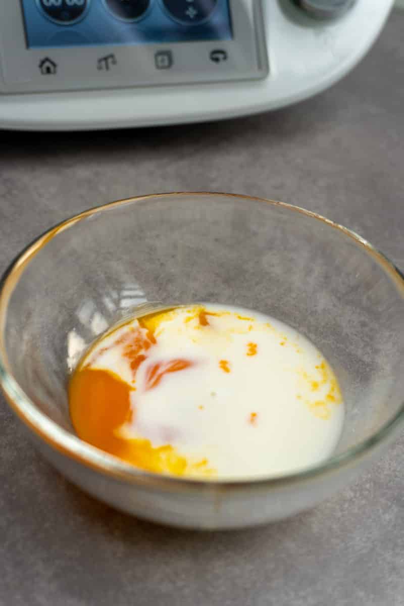 Egg yolk being tempered in a cup with warm milk