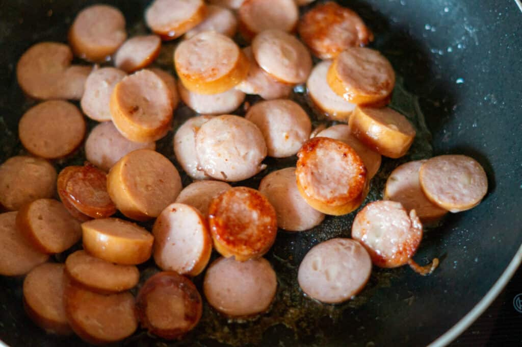 Sliced smoked pork sausage being fried in a pan