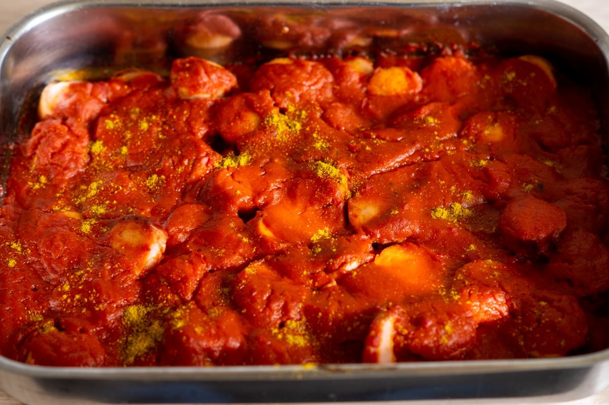 Currywurst baking in the oven with sauce poured over the sausage slices