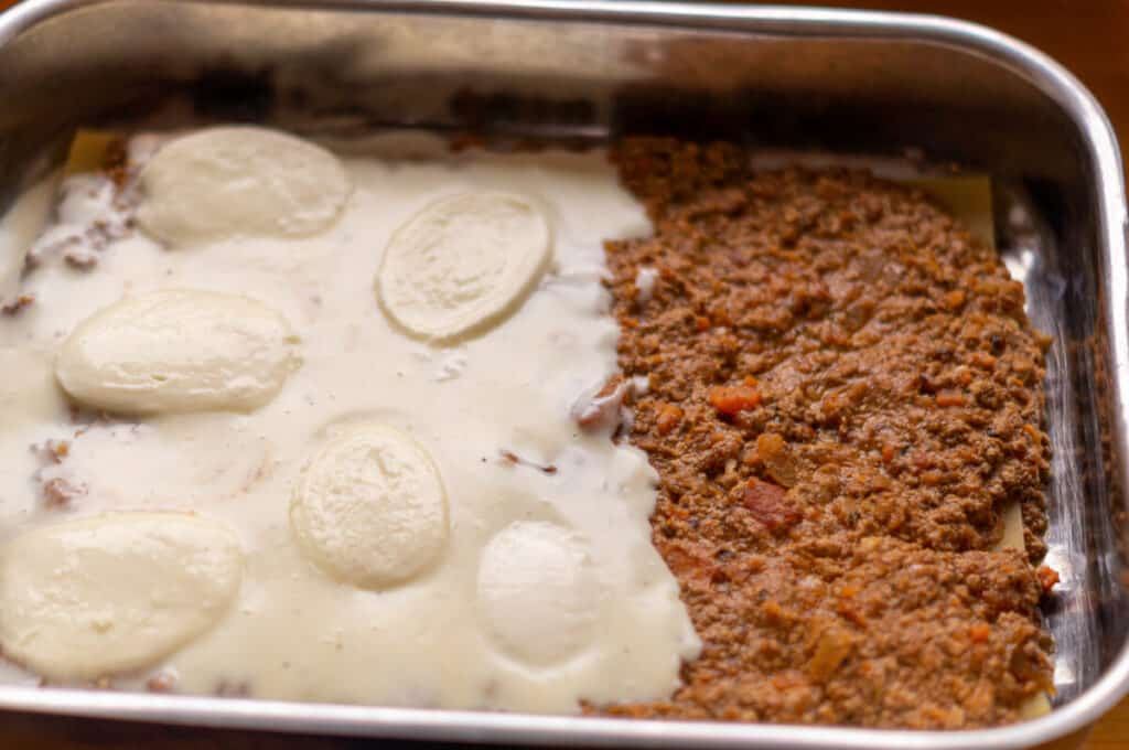 The ingredients for the lasagne being layered alternately in the baking dish