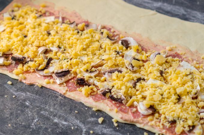 Rolled-out pizza dough topped with Crème fraîche sauce, Gouda, mushrooms and salami
