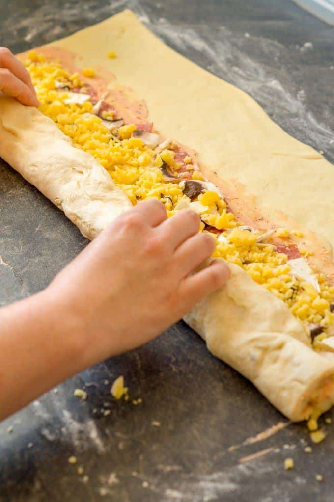 Pizza dough with filling being rolled up from the long side