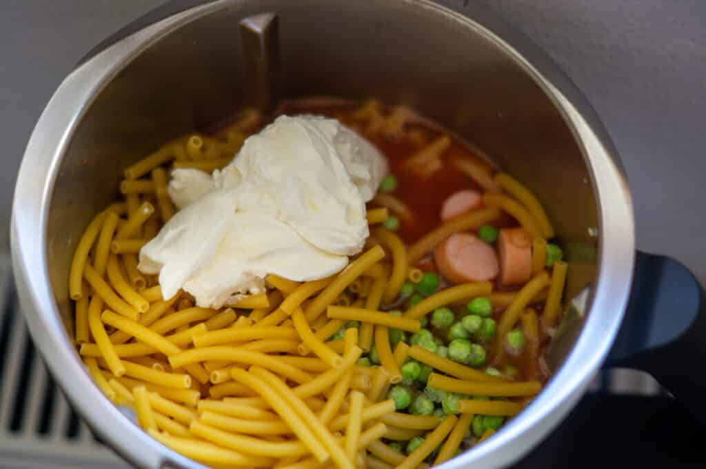 Adding pasta, vegetables, sausages and soured cream to the mixing bowl